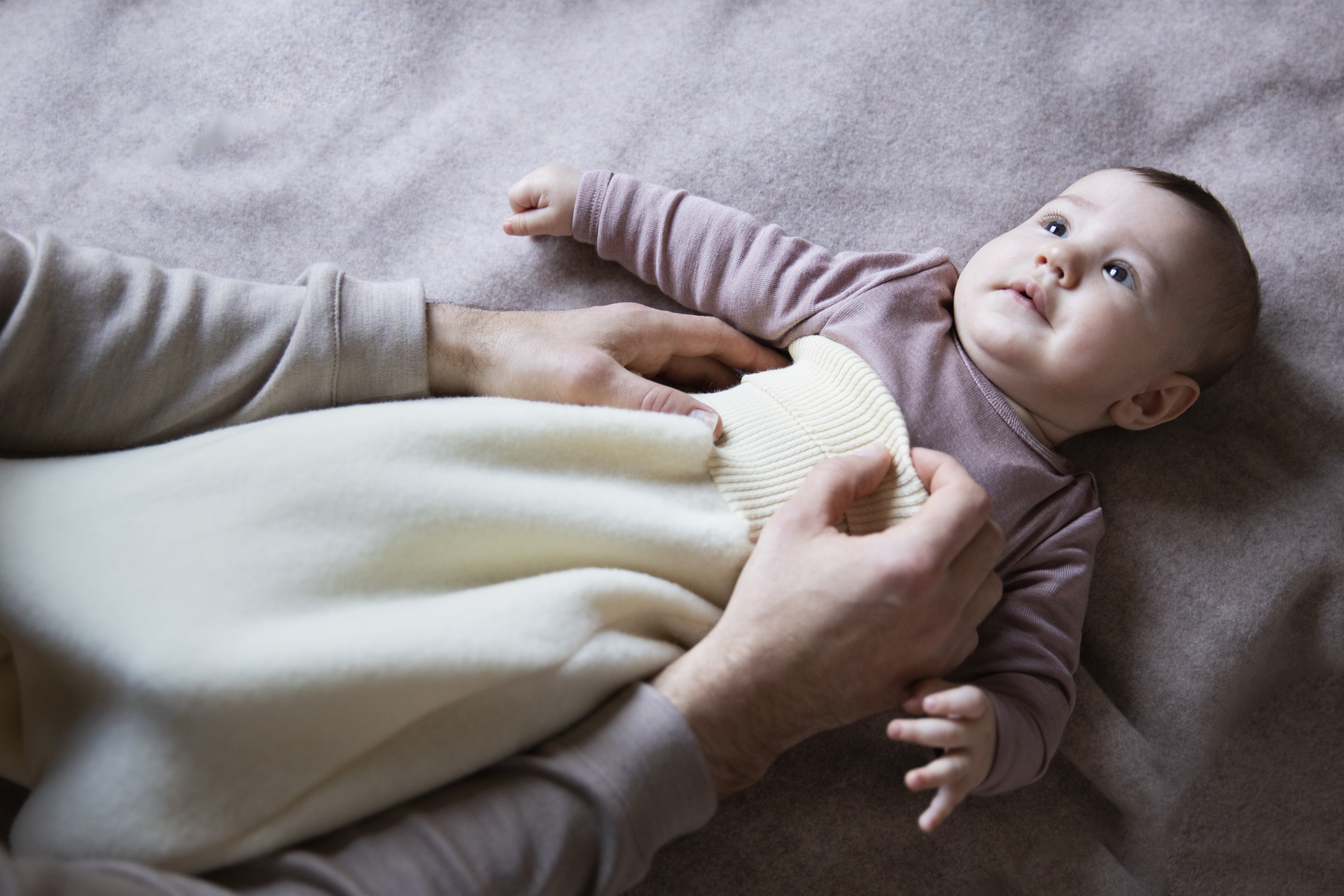 Baby wird von Papa mit Engel Schlafsack aus Merinowolle angezogen.